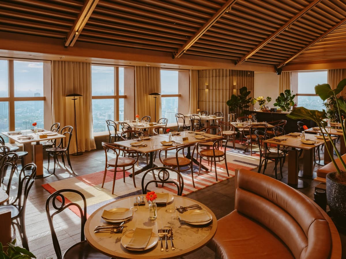Dining room at SKYE Rooftop Dining & Lounge with tan leather seating and Jakarta skyline views.